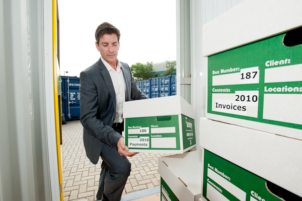 Man in a suit carrying a box of invoices into a storage container.